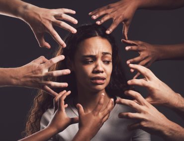 Shot of hands grabbing a young womans against a dark background.